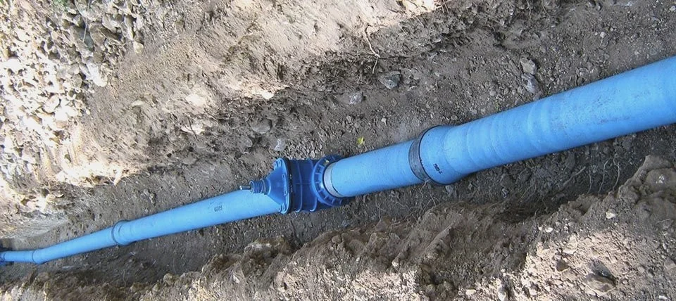 Im Erdreich verlegte blaue Versorgungsleitung mit Anschlussarmaturen.